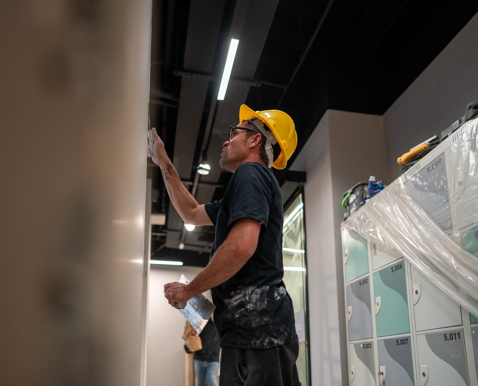 Profissional da ArqYou executando acabamento de parede em obra corporativa